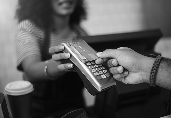 A person pays for a coffee in a coffee shop by holding a contactless card at a card machine held by a cashier.