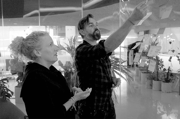 Two members of the Equal Experts network mapping a process at a whiteboard with post-it notes